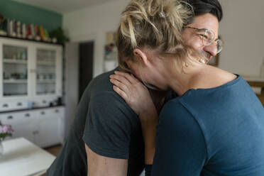 Happy couple embracing in kitchen at home - KNSF07666