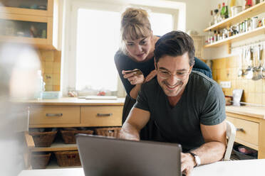 Happy couple shopping online in kitchen at home - KNSF07673