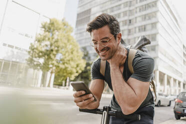 Lässiger Mann mit E-Scooter, der in der Stadt sein Smartphone überprüft - KNSF07677