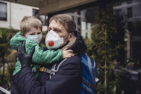 Vater mit Sohn, beide mit Schutzmaske, im Freien, lizenzfreies Stockfoto