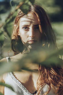 Porträt einer rothaarigen Frau mit Nasenpiercing zwischen Zweigen, die in die Kamera schaut - MTBF00356