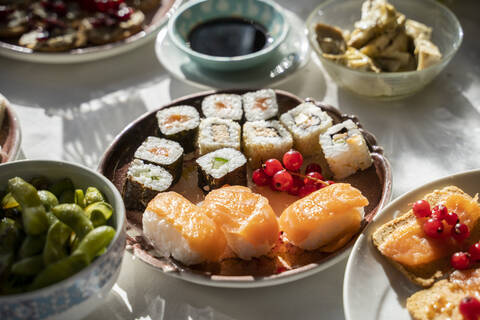 Spanien, Teller mit verzehrfertigem Sushi auf gedecktem Esstisch, lizenzfreies Stockfoto