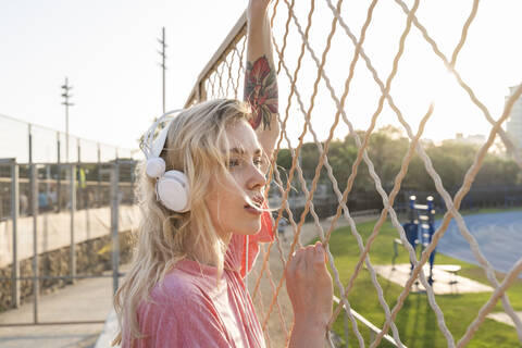 Junge Frau hört Musik an einem Maschendrahtzaun, lizenzfreies Stockfoto