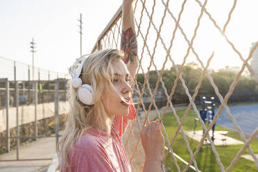 Junge Frau hört Musik an einem Maschendrahtzaun - AFVF05487
