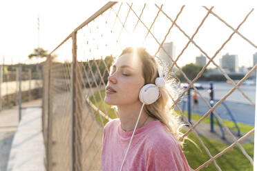 Junge Frau hört Musik an einem Maschendrahtzaun - AFVF05488