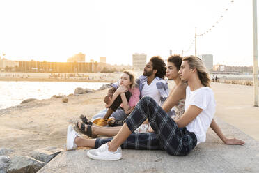 Friends sitting on quay wall at sunset - AFVF05497