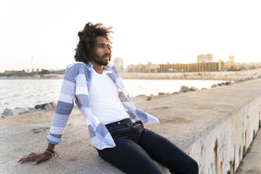 Young man sitting on quay wall at sunset - AFVF05503