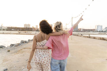 Rückansicht von zwei jungen Frauen auf der Uferpromenade bei Sonnenuntergang - AFVF05516