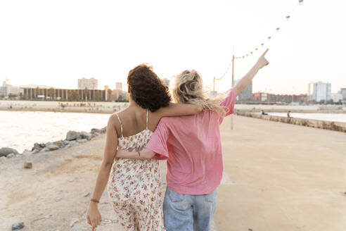 Rückansicht von zwei jungen Frauen auf der Uferpromenade bei Sonnenuntergang - AFVF05516