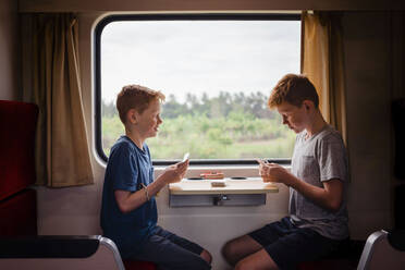 Side view of boys playing cards while traveling in train, Thailand, Asia - NMSF00408