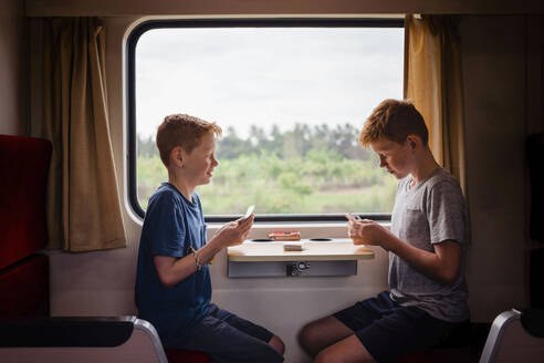 Seitenansicht von Jungen, die Karten spielen, während sie im Zug unterwegs sind, Thailand, Asien - NMSF00408