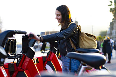 Young woman catching a red rental bike. - CAVF75890