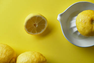 Auspressen einer Zitrone in einer weißen Keramik-Saftpresse auf gelbem Hintergrund - CAVF75910