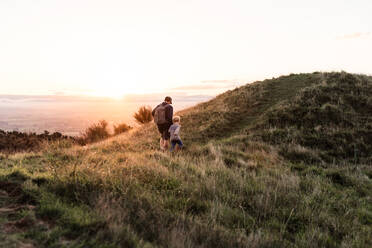 Vater und Sohn wandern in der Abenddämmerung auf einem Hügel - CAVF75944