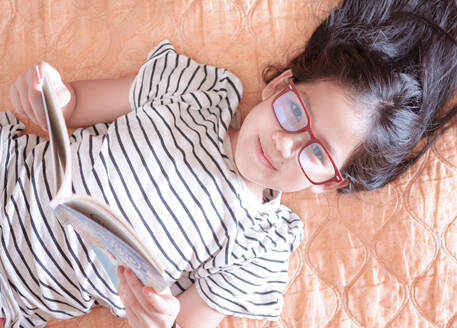 A girl lying down reading a book on a weekend - CAVF75952