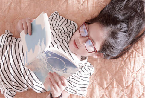 A girl lying down reading a book on a weekend - CAVF75953