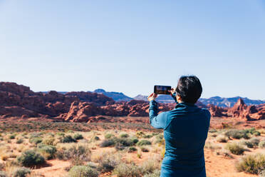 Senior Asian woman taking a photo of a desert landscape with her camer - CAVF75978