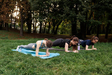 Die entspannten Mädchen machen Yoga im Park auf dem Teppich - CAVF76000