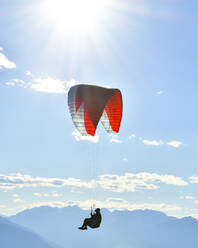 Paraglider flying in blue skies with sunflare - CAVF76044