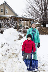 Ein Mädchen im Teenageralter und ihr 6 Jahre alter Bruder posieren mit einem Schneemann - MINF14040