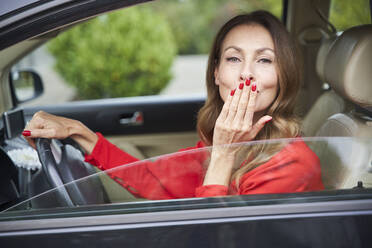 Portrait of smiling mature woman in car blowing a kiss - PNEF02470