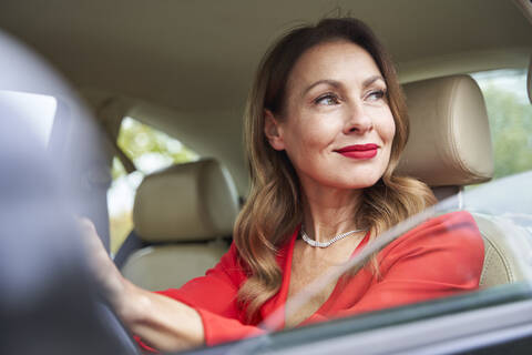 Porträt einer lächelnden reifen Frau, die aus dem Autofenster schaut, lizenzfreies Stockfoto