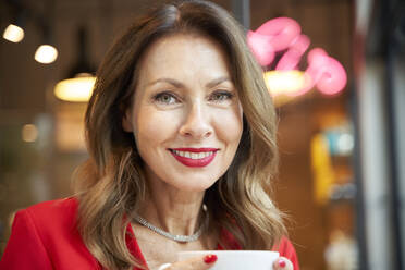 Porträt einer lächelnden reifen Frau mit einer Tasse Kaffee in einem Cafe - PNEF02484