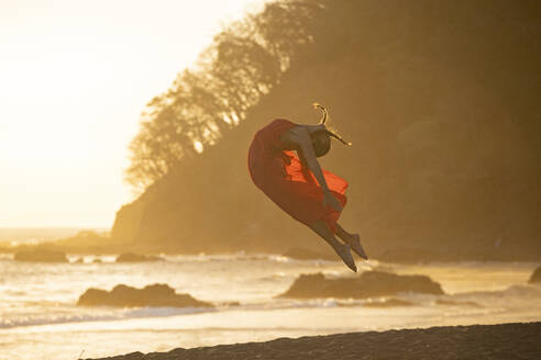 Teenager-Mädchen im roten Kleid übt Gymnastik am Meer bei Sonnenuntergang, Jaco Beach, Costa Rica - AMUF00009