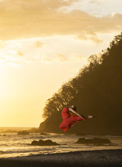 Teenager-Mädchen im roten Kleid übt Gymnastik am Meer bei Sonnenuntergang, Jaco Beach, Costa Rica - AMUF00010