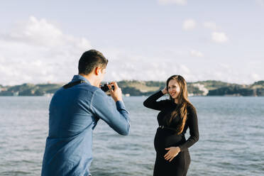 Young man photographing his pregnant girlfriend at the waterfront - DCRF00049