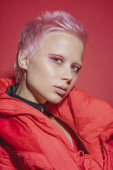 Porträt einer jungen Frau mit kurzen rosa Haaren und roter Jacke vor rotem Hintergrund - VPIF02120