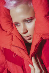 Porträt einer jungen Frau mit kurzen rosa Haaren und roter Jacke vor rotem Hintergrund - VPIF02121