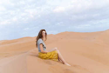 Porträt einer rothaarigen jungen Frau auf einer Sanddüne in der Wüste Sahara, Merzouga, Marokko - AFVF05536