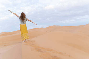 Junge Frau steht mit ausgestreckten Armen auf einer Sanddüne in der Wüste Sahara, Merzouga, Marokko - AFVF05537