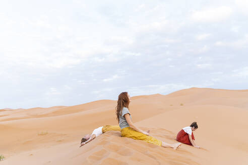 Drei junge Frauen ruhen sich auf einer Sanddüne in der Wüste Sahara aus, Merzouga, Marokko - AFVF05541