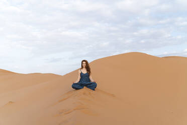 Junge Frau sitzt auf einer Sanddüne in der Sahara-Wüste und übt Yoga, Merzouga, Marokko - AFVF05546