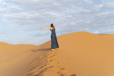 Junge Frau steht mit ausgestreckten Armen auf einer Sanddüne in der Wüste Sahara, Merzouga, Marokko - AFVF05550