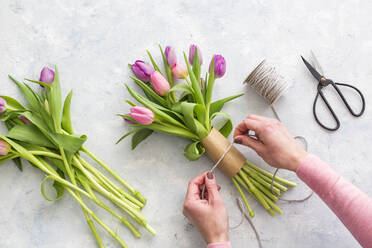 Hände einer Frau bereiten einen Strauß lila blühender Tulpen vor - JUNF01756
