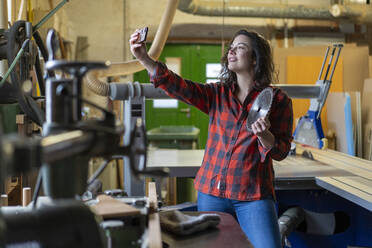 Handwerkerin hält Sägeblatt und macht ein Selfie in ihrer Werkstatt - MOEF02805