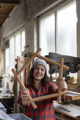 Lächelnde Schreinerin hält ein Werkstück in ihrer Werkstatt - MOEF02812