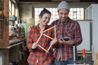 Porträt einer glücklichen Handwerkerin und eines Handwerkers mit Tafel und Maßstab in ihrer Werkstatt - MOEF02836