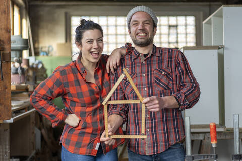 Porträt einer glücklichen Handwerkerin und eines Handwerkers, die in ihrer Werkstatt einen Zollstock halten, lizenzfreies Stockfoto