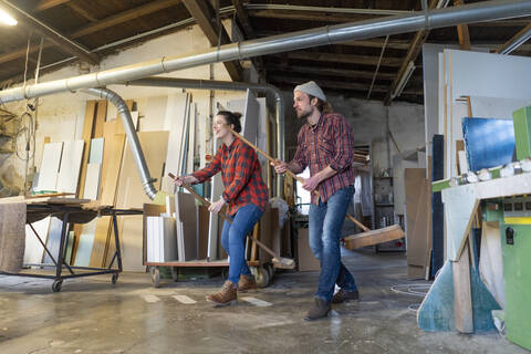 Playful craftswoman and craftsman riding on brooms in their workshop stock photo