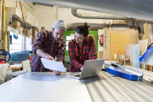 Handwerkerin und Handwerker mit Plan und Laptop bei der Diskussion in ihrer Werkstatt - MOEF02840