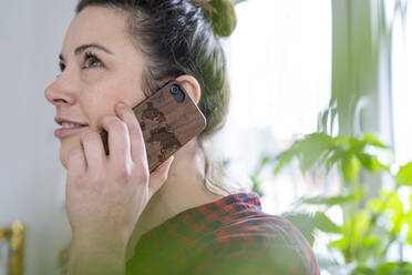 Porträt einer lächelnden Frau, die ein Holzhandy benutzt - MOEF02845