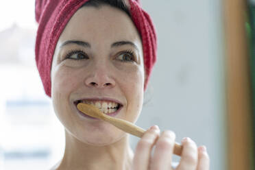 Porträt einer Frau mit in ein Handtuch gewickeltem Kopf, die sich mit einer Holzzahnbürste die Zähne putzt - MOEF02857