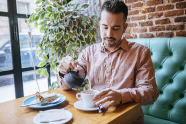 Mann in einem Café gießt Tee in eine Tasse - KIJF02924