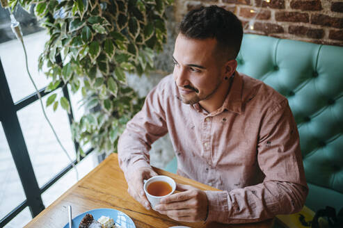 Mann in einem Café mit einer Tasse Tee und Blick aus dem Fenster - KIJF02931