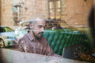 Mann hinter der Fensterscheibe eines Cafés mit Laptop - KIJF02937