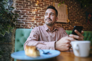 Portrait of a man in a cafe holding cell phone - KIJF02943